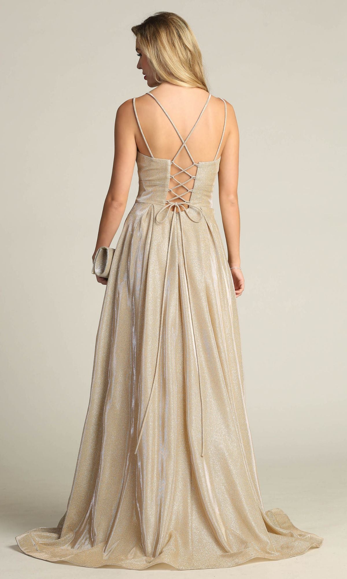 A woman stands facing away, holding a small clutch, in the Lace-Up Back Long Metallic A-Line Prom Dress 4022 featuring shimmering gold fabric, a corset lace-up back, and crisscross straps.